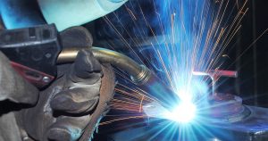 Welding services in Southeastern PA. The image shows a welder working on a metal structure, with bright welding sparks flying and protective gear visible in an industrial workshop or construction site.