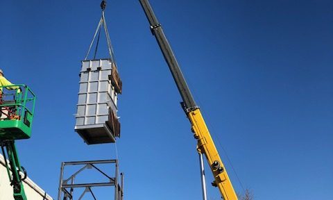 Heat exchanger being installed and rotated into position. The image shows a large heat exchanger being carefully maneuvered into place with the help of rigging equipment and cranes, with workers overseeing the installation.