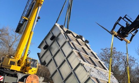 Heat exchanger tipped and rotated. The image shows a large heat exchanger in a tilted position, being adjusted or rotated into place with the help of rigging equipment and construction machinery.