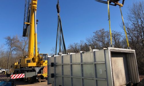 Rigging a heat exchanger. The image shows workers using rigging equipment to lift and position a large heat exchanger, with cranes and other construction machinery in the background."