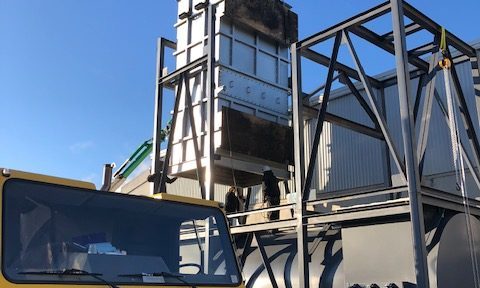 Installing a heat exchanger The image shows workers positioning, rotating, setting and securing a large heat exchanger into place, with rigging equipment and construction machinery visible in the background.