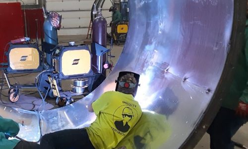 MJ Nester specialty welding contractors at work. The image shows a welder in protective gear performing welding tasks on a metal structure, with bright sparks visible, highlighting the precision and skill involved in the welding process.