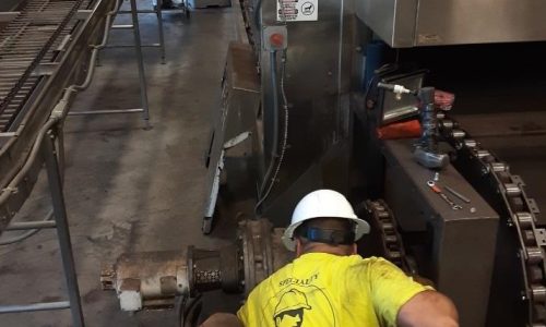 A construction worker kneeling and working on a metal structure at an industrial site. The image shows the worker in safety gear focused on securing or adjusting parts of the structure with tools nearby.